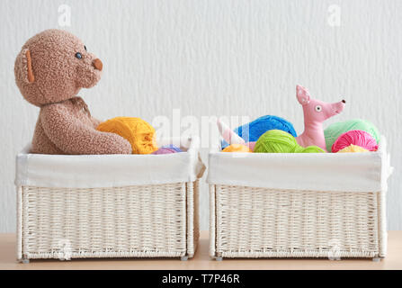 Weidenkörbe mit Kugeln von strickgarn und lustiges Spielzeug auf Tisch gegen hellen Hintergrund Stockfoto