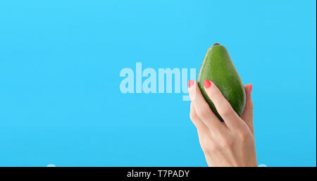 Avocado in der Hand von Frau blau hintergrund Stockfoto