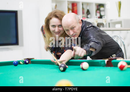 Ein älterer Mann mit einer Frau Billard spielen. Späte Liebe. Rentner, flirtet mit einem Mädchen. graues Haar in einen Bart und ein Dämon in eine Rippe Stockfoto