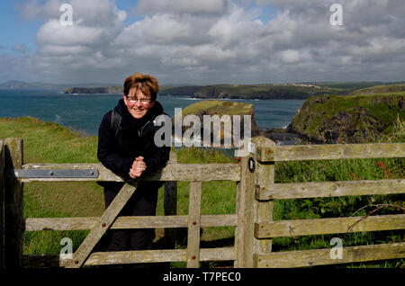 Happy Walker schiefen über eine hölzerne Tor auf der Pembrokeshire Coast Path, in der Nähe von Porthgain an einem hellen Tag, mit der dramatischen Küste im Hintergrund Stockfoto