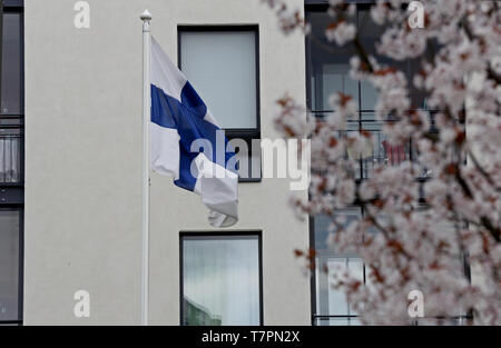 Finlands Fahne in der Luft an einem Frühlingstag vor einem Mehrfamilienhaus mit Cherry Park fliegen Stockfoto