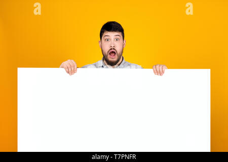 Überrascht Mann hält ein Banner für Text bärtigen, ausdrucksstarken Shouts und einladenden Käufer Stockfoto