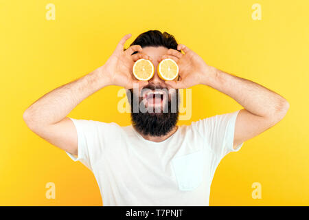 Bärtiger hippie Mann mit Zitronenscheiben vor Augen, auf gelben Hintergrund. Stockfoto