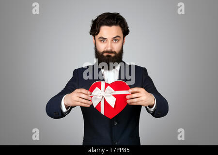 Bärtige Geschäftsmann hält Geschenk über grauer Hintergrund Stockfoto