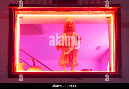 Ein furchtsames Schaufenster mit einem Baby Puppe in einem Schaufenster, Rosa und Gelb Neonröhren fügen Sie diesem Halloween suchen Anzeige Stockfoto