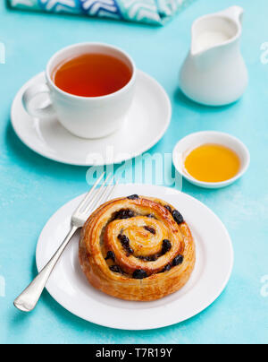 Frischen dänischen Gebäck mit Rosinen und einer Tasse Tee auf der blauen Tabelle Hintergrund. Stockfoto