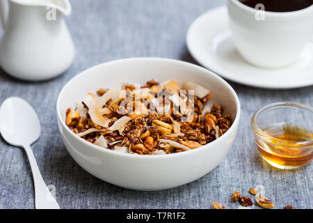 Gesundes Frühstück. Frisches Müsli, Müsli mit Kokos, Banane und Nüsse in einer weißen Schüssel auf graue Background. Stockfoto