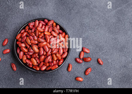 Rote Linsen in einem schwarzen Schüssel auf grauem Stein Hintergrund. Ansicht von oben. Kopieren Sie Platz. Stockfoto