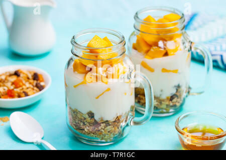 Frische mango Obst mit Joghurt und Müsli in Töpfen. Blauer Stein Hintergrund. Close Up. Stockfoto