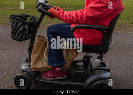 Eine Seite, auf der eine ältere Dame in einem roten Mantel, in der Freiheit eines elektrischen Mobilität scooter, von den Schultern nach unten Stockfoto