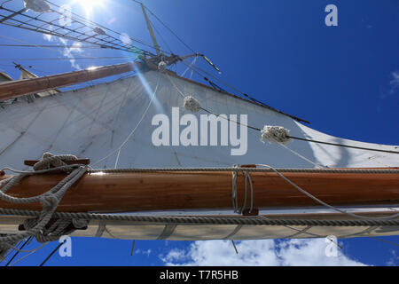 Eine niedrige Winkel Ansicht einer Tall Ship Segeln gegen einen strahlend blauen Himmel, die unternommen wurden, um die vom Deck des Bootes, Sun flare über der Oberseite des Segels kommen Stockfoto