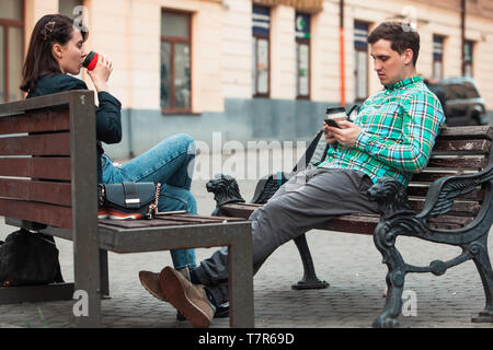 Kommunikationsproblem Mann mit Frau sitzt auf der Bank an der Strasse der Stadt trinken Kaffee im Pappbecher suchen ito Telefone. lifestyle Konzept. schüchtern zu sprechen Stockfoto