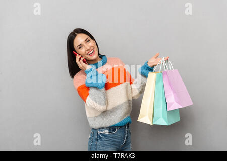 Portrait von positive Frau 30 s tragen bunte Papier Einkaufstüten und Gespräch am Handy isoliert über grauer Hintergrund Stockfoto