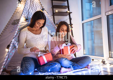 Foto eines glücklichen jungen Frau mit ihrer kleinen Tochter Mädchen Spaß am Boden Betrieb vorhanden Geschenkboxen. Weihnachten Konzept. Stockfoto