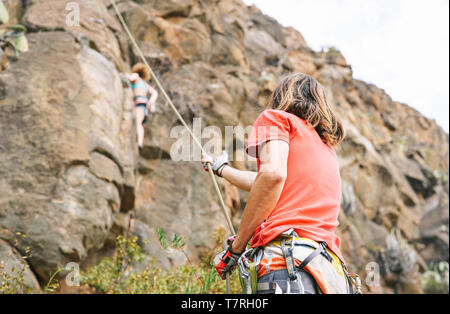 Menschen Hilfe zu geben, Frau, die ist Klettern am Berg Cliff - Bergsteiger in Aktion auf hohen Felsen - Begriff der Extreme Sport Lifestyle Menschen Stockfoto