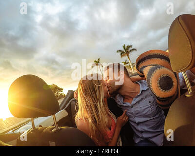 Trendige junge Paar in ein bewegender Moment im Cabrio während ihres Ausflugs - Glückliche romantischen Jungvermählten Datum Küssen in Cabriolet Auto Stockfoto