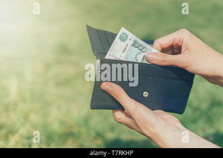 Die Hände schließen nimmt eine Banknote der Russische Rubel aus der Brieftasche auf grünem Hintergrund außerhalb Stockfoto