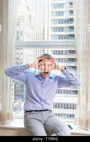 Junge Unternehmer sitzen auf Fensterbank in Dress Shirt betont, Hände auf den Kopf und offenem Mund an der New York City in Manhattan im Hotel für Interview Stockfoto