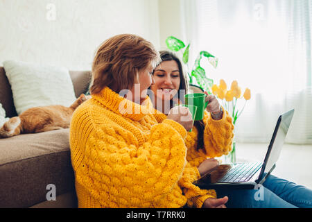 Ältere Mutter und ihre erwachsenen mit Laptop zu Hause, während das Trinken von Tee Tochter. Muttertag Konzept. Stockfoto