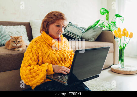 Ältere Frau mit Laptop zu Hause entspannen mit Katze. Ältere Menschen lernen moderne Technologie Stockfoto