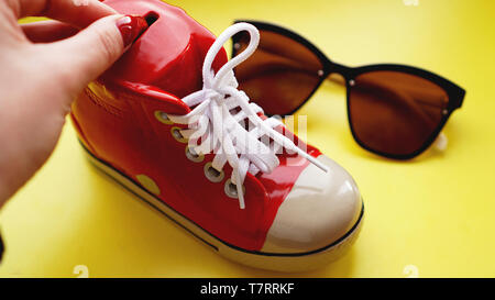 Kässeli in Form von Sneakers. Sonnenbrille auf gelbem Hintergrund. Das Konzept der Einsparungen auf Urlaub und Sommerferien. Geld sparen Stockfoto