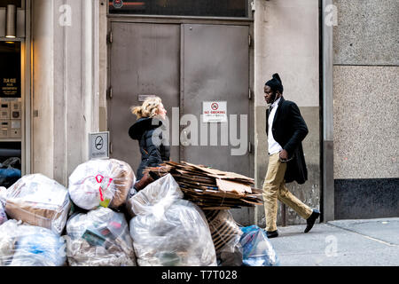 New York City - 6. April 2018: Leute, die viel zu Fuß auf Gehweg Pflaster durch Haufen Müll Müll in New York Midtown Stockfoto