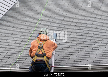 Haus während des Tages mit grauer Farbe Einfamilienhaus und Mann zu Fuß auf Dachschindeln und Leiter während der Reparatur Stockfoto