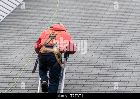 Haus während des Tages mit grauer Farbe Einfamilienhaus und Bau Mann in Uniform zu Fuß auf Dachschindeln und Leiter während der Reparatur Stockfoto