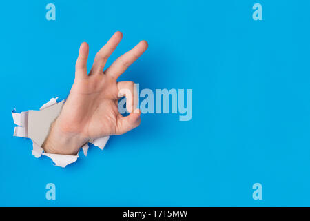 Männliche Hand reißen durch blaues Papier Hintergrund erstellen ok Geste mit der Hand und kopieren Sie Platz für Text. Stockfoto