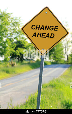 Ein gelbes Warnsymbol Straße Zeichen, das sagt "ÄNDERN". Das Zeichen ist eine Metapher. Das Schild befindet sich neben einer asphaltierten Landstraße. Stockfoto