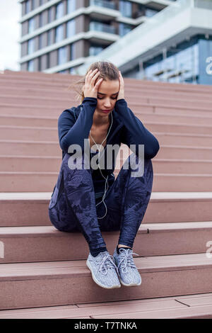 Sorgen junge sportliche Frau sitzt auf der Treppe Stockfoto