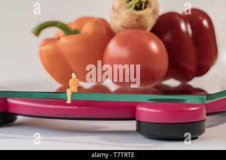 Miniatur Frau Abbildung verlegen auf die digitale elektronische Personenwaage, die für das Gewicht des menschlichen Körpers. Frisches Gemüse bei geringer Tiefenschärfe Hintergrund Stockfoto