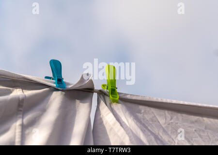 Weiße Kleidung hingen auf einer Wäscheleine zum Trocknen und durch die Kleidung befestigt Pflöcke gegen den blauen Himmel im hellen warmen sonnigen Tag Stockfoto