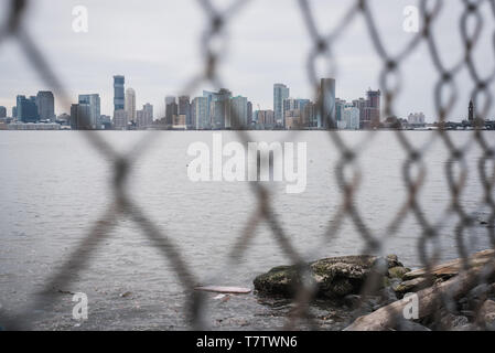 Manhattan Skyline Blick durch einen Zaun entlang dem Hudson River Greenway in New York durch einen blauen Himmel Frühjahr Stockfoto