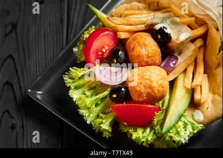 Gyros in Pita mit Falafel, Oliven und Feta. Traditionelle griechische und jüdische Küche Teller. gesundes Mittagessen an der schwarzen Holz- Kulisse. Nahaufnahme Stockfoto