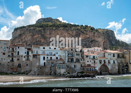 Historische Häuser am Strand mit La Rocca hinter in der malerischen Altstadt von Cefalu, Sizilien. Stockfoto