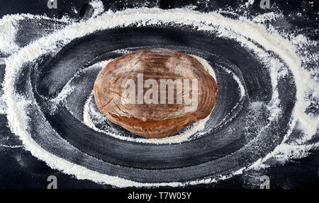 Gebackenes Brot und weißes Mehl von Weizen auf einem Schwarzen Tisch verstreut, Ansicht von oben Stockfoto