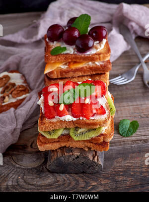 Stapel der French Toast von Weißbrot mit Hüttenkäse, Erdbeeren, Kiwis, Kirschen auf einem grauen Holzbrett Stockfoto