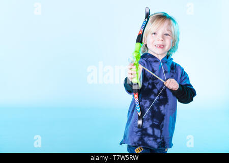 Junger kaukasischer Junge in blauem T-Shirt auf blauem Hintergrund mit Schleife und Pfeil Stockfoto