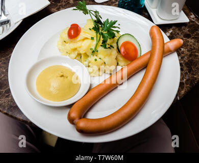 POV an der Platte mit zwei traditionelle Deutsche lange Würstchen und Kartoffelsalat mit Gemüse und Senf Platte Stockfoto