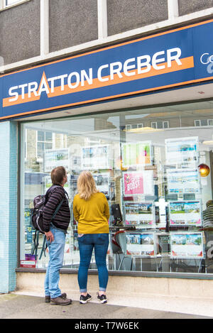 Die Leute, die auf der Suche nach Eigentum Informationen in einem Stratton Creber Immobilienmakler Fenster im Stadtzentrum von Newquay in Cornwall. Stockfoto