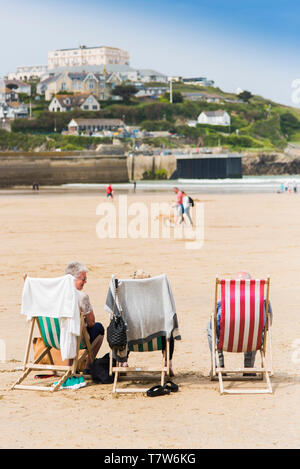 Urlauber in Liegestühlen in der Sonne auf den Towan Strand in Newquay in Cornwall sitzen. Stockfoto