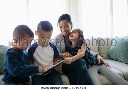 Glückliche Mutter und Kinder mit digitalen Tablette auf Sofa im Wohnzimmer