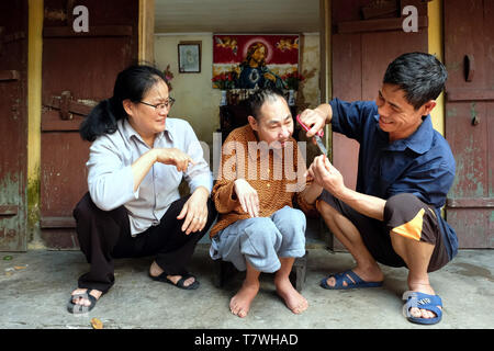 Die katholische Schwester Marie Binh (55) aussieht, nachdem der Agent Orange Opfer Minh lange Nguyen (64), lebt mit seinem nächsten Van Hung (54, rechts). Phu Ly Dorf (Ha Nam Provinz) in der Nähe von Hanoi, Vietnam Stockfoto