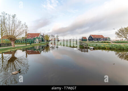 ZAANSE SCHANS, 14. April 2019 - Reflexion der Holz- grüne Häuser mit dunklen orange Farbe Dach auf dem ruhigen Wasser des Kanals wider Stockfoto