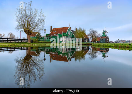 ZAANSE SCHANS, 14. April 2019 - Reflexion der Holz- grüne Häuser mit dunklen orange Farbe Dach auf dem ruhigen Wasser des Kanals wider Stockfoto