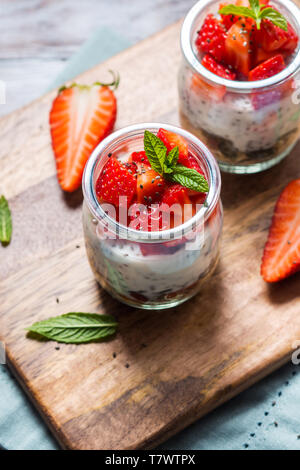 Joghurt Müsli Parfait mit Erdbeeren und Chia Samen. Gesunde Single-portion-Frühstück serviert im Glas Tassen auf Holzbrett mit grünen Serviette. Natu Stockfoto