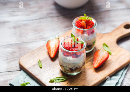 Joghurt Müsli Parfait mit Erdbeeren und Chia Samen. Gesunde Single-portion-Frühstück serviert im Glas Tassen auf Holzbrett mit grünen Serviette. Natu Stockfoto