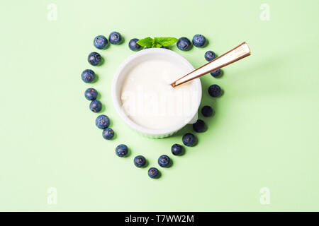 Schüssel Naturjoghurt und frische Blaubeeren in Form von Herzen auf Pastell grün hinterlegt. Gesundes Frühstück Konzept Stockfoto