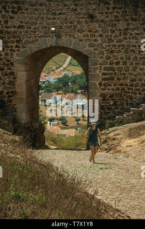 Frau zu Fuß durch das Gateway auf Mauer aus Stein, die in der Straße von evoramonte. Eine kleine Stadt mit Marmor bauten auf Osteuropa Portugal. Stockfoto